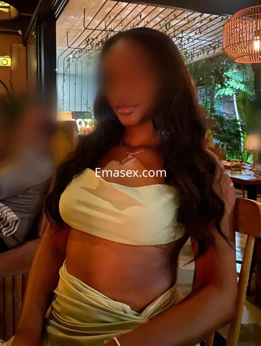 Escort en Pamplona con cabello largo y ondulado, vistiendo un top claro y posando en un ambiente acogedor y elegante.