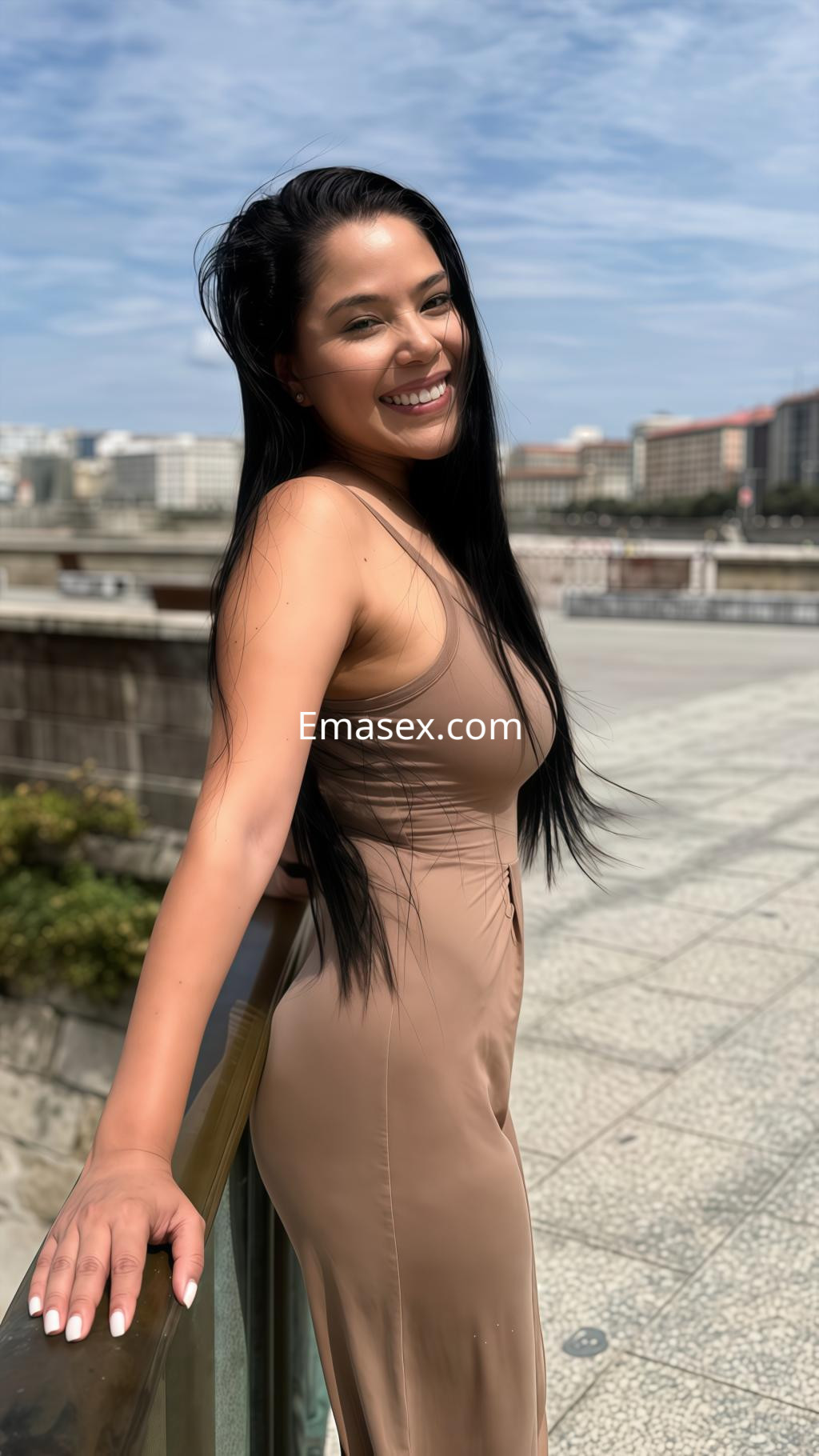 Escort en Coruña, posando de pie junto a una barandilla con un vestido largo beige, sonriendo con confianza.