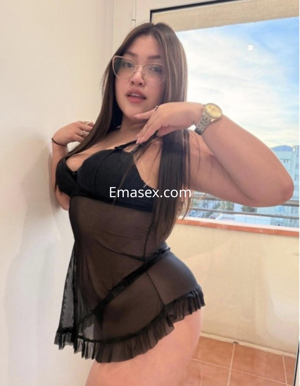Puta en Vitoria viste un conjunto de lencería negra transparente y gafas, posando con sensualidad.