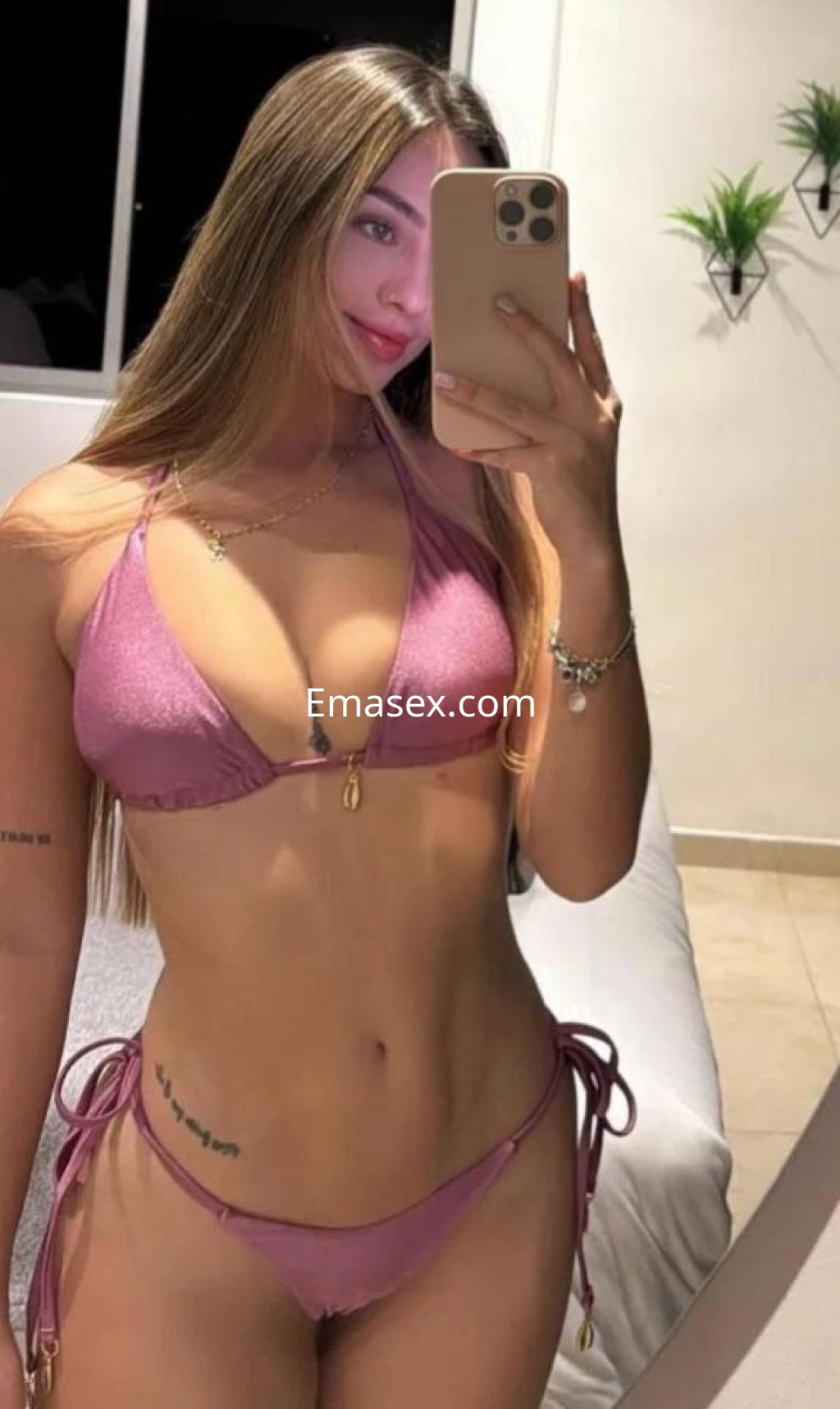 Escort en Coruña con cabello largo y lacio, viste un bikini rosa y posa frente a un espejo en un ambiente luminoso.