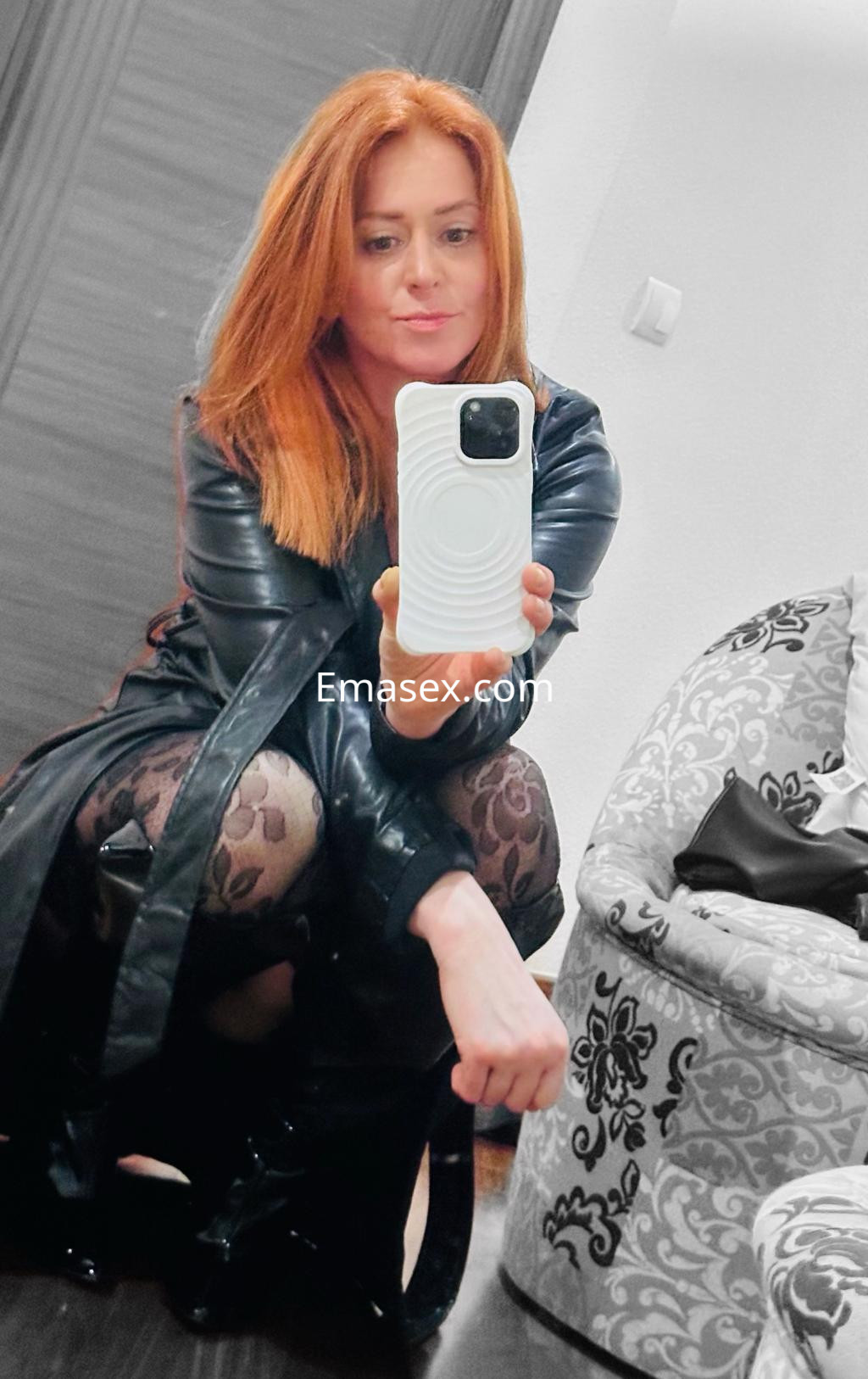 Puta en Santander, con cabello largo y pelirrojo, viste abrigo de cuero y medias con diseño, tomando una selfie.
