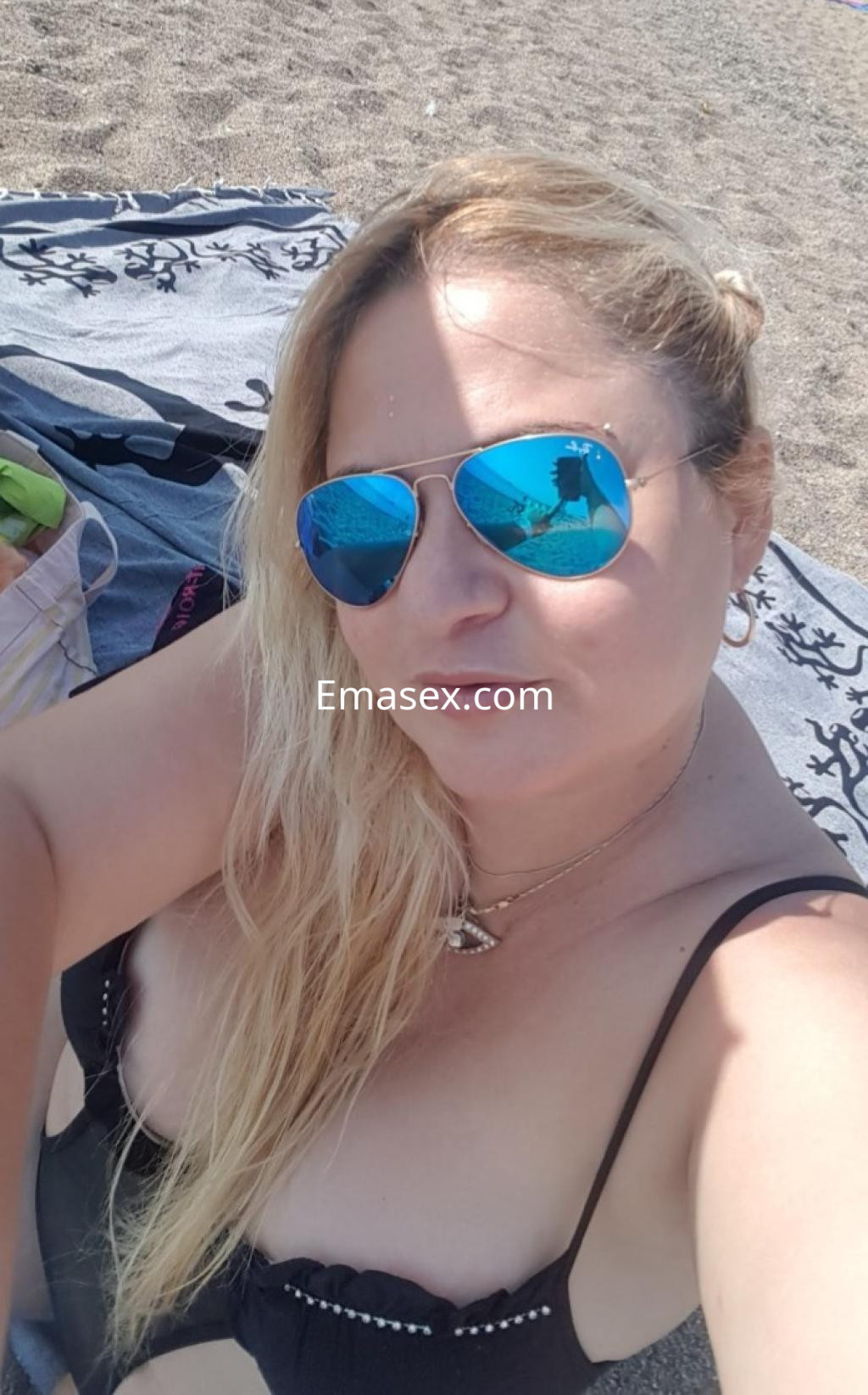 La puta en Lleida se toma una selfie en la playa, luciendo un bikini negro y gafas de sol.