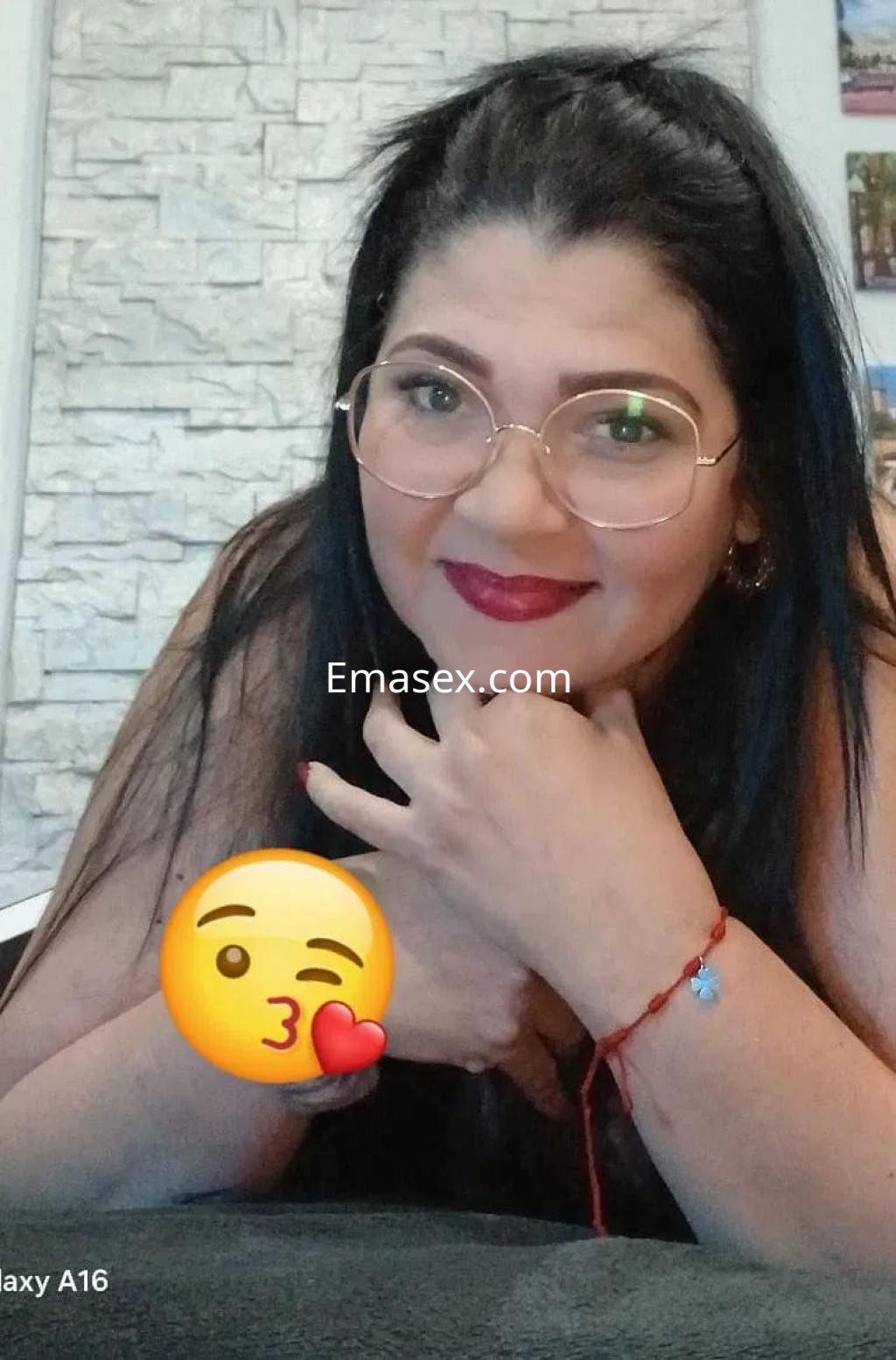 Escort de cabello oscuro y lacio, con gafas y maquillaje sutil, posando en un entorno interior en Alicante.
