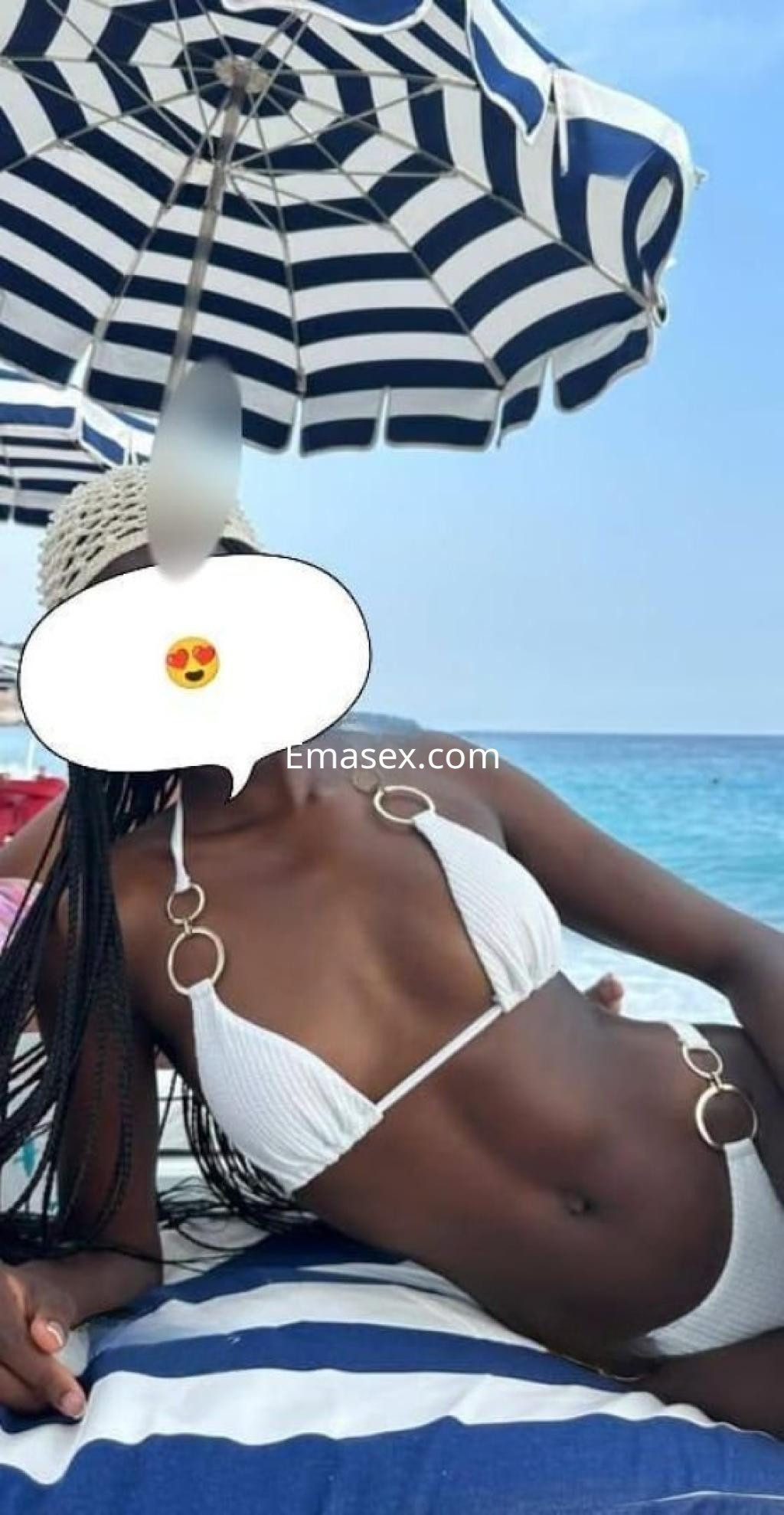 La escort se relaja en la playa de Badajoz, vistiendo un bikini blanco y bajo una sombrilla a rayas.