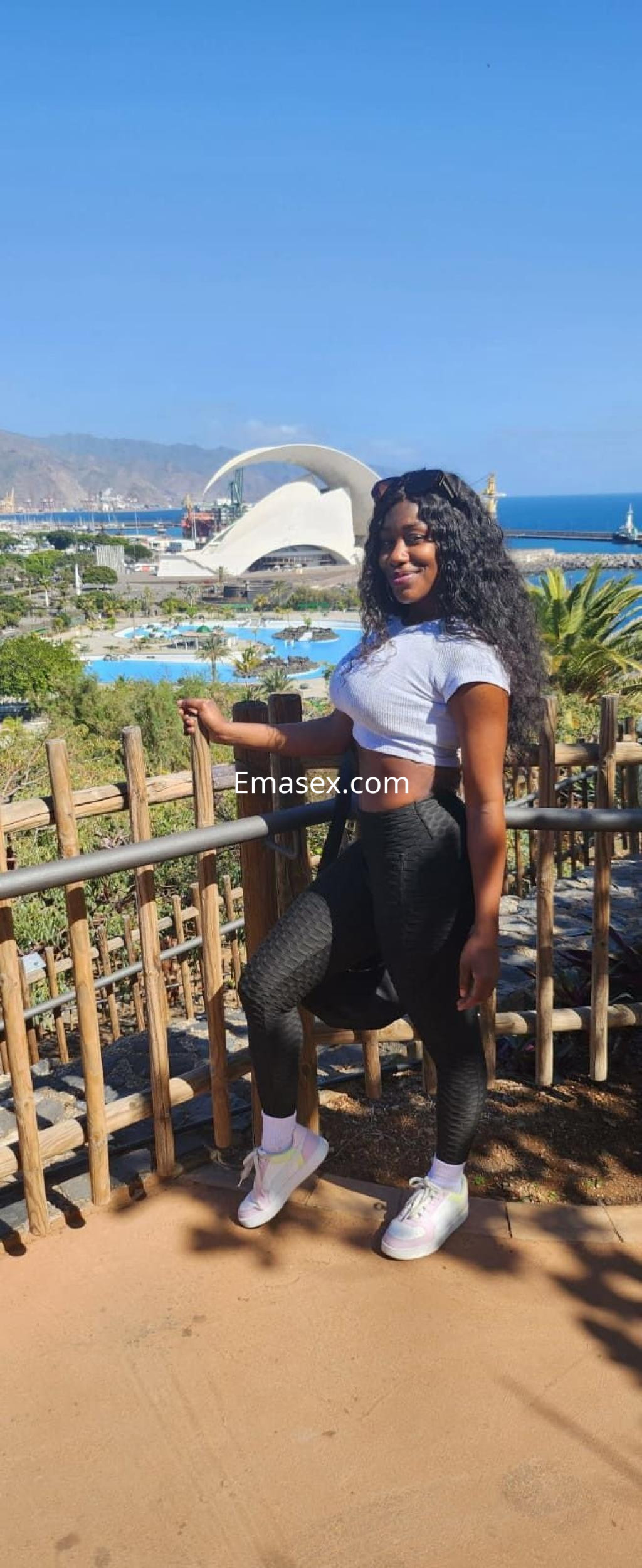 Puta posando en Palma de Mallorca, con cabello rizado y negro, luciendo un top blanco y leggings oscuros.