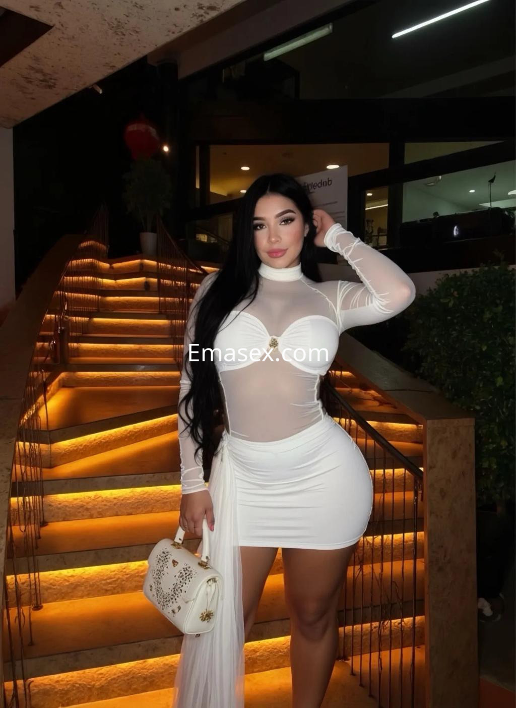 Puta posando con un vestido blanco ajustado y transparente, luciendo elegante en una escalera iluminada en Palma de Mallorca.