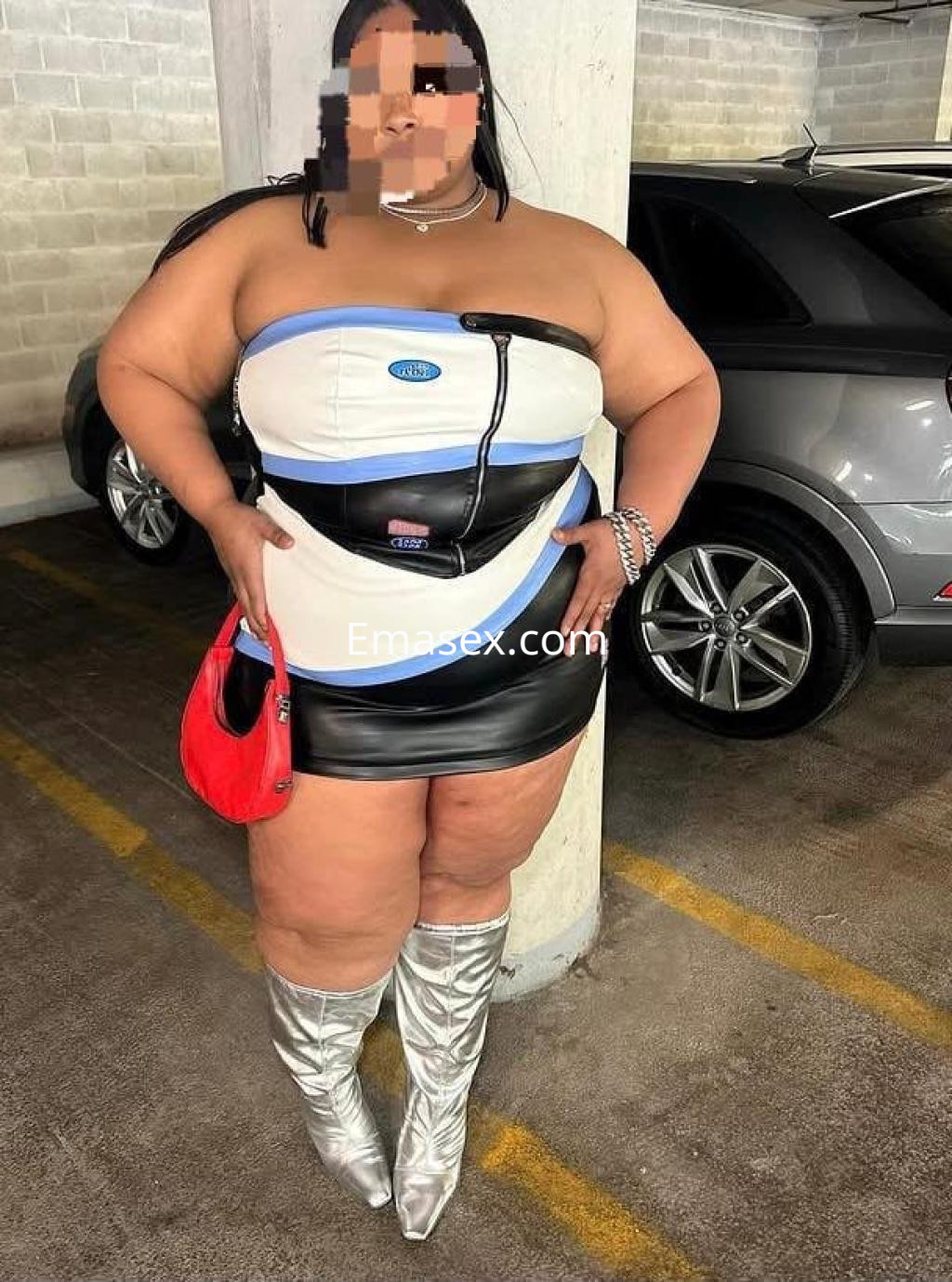 Escort en Girona luciendo un ajustado vestido negro y blanco con botas plateadas en un aparcamiento.