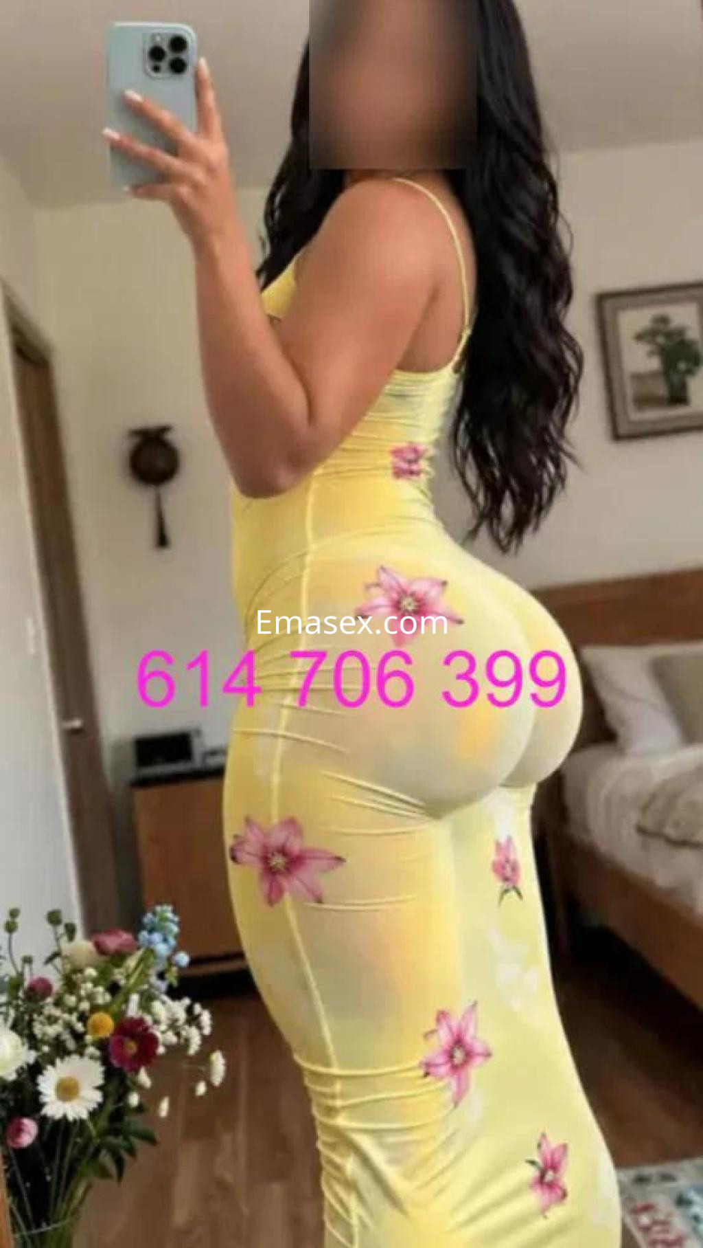Escort en Granada, vestida con un vestido amarillo ajustado y flores, posando de perfil en un ambiente interior.