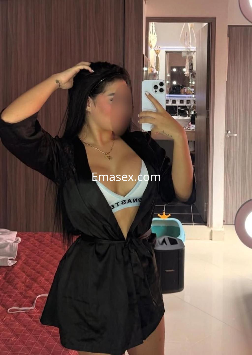 Escort en Murcia con cabello largo y oscuro, vistiendo una bata negra sobre lencería blanca, posando en un espejo.