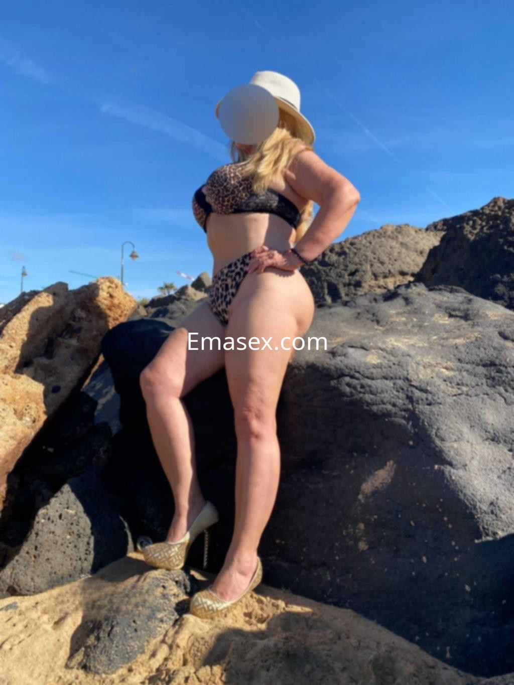 La puta posa de pie sobre rocas en la playa de Tenerife, luciendo un bikini de leopardo y tacones.