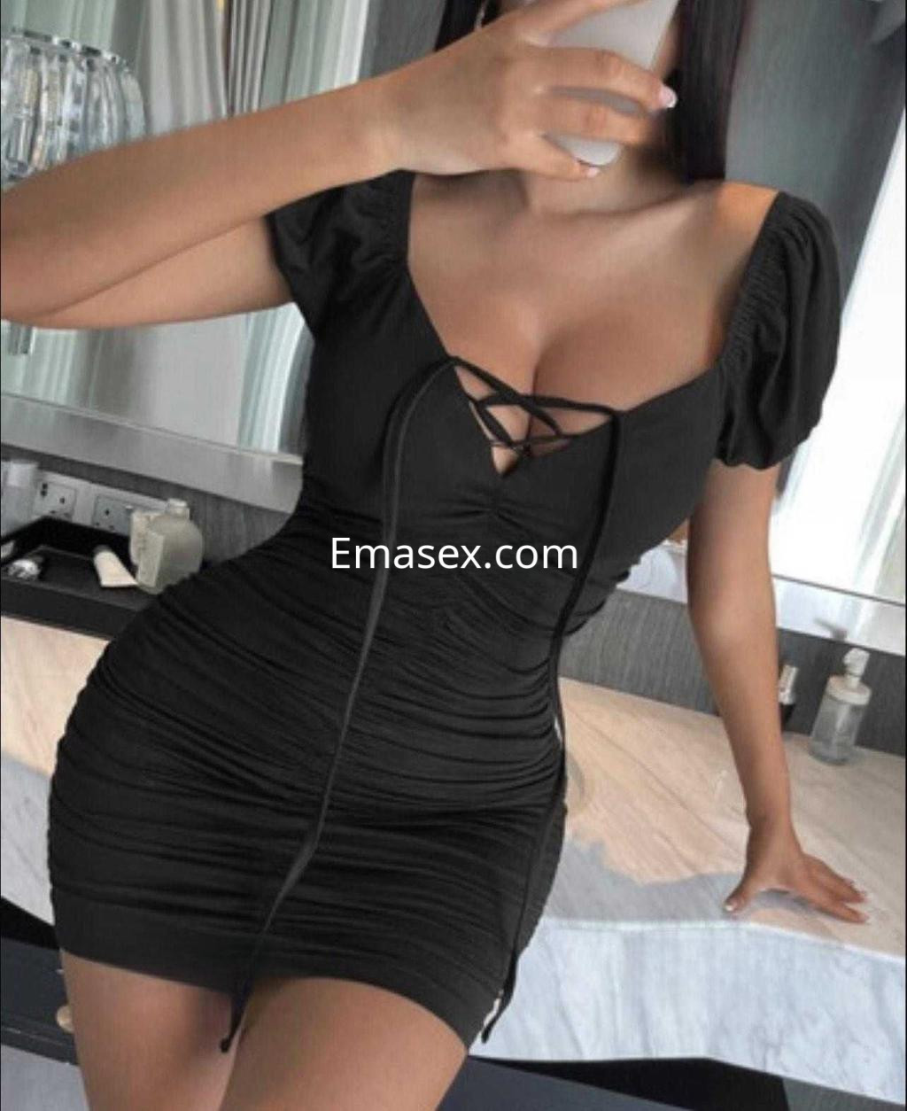 Puta en Toledo viste un ajustado vestido negro con detalles de encaje, posando frente a un espejo.