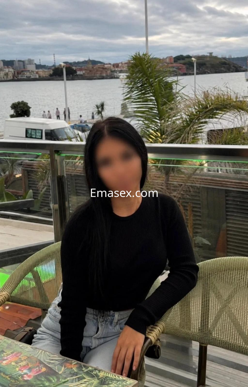 Puta de cabello largo y lacio, viste un suéter negro y jeans, sentada en una terraza en Oviedo.