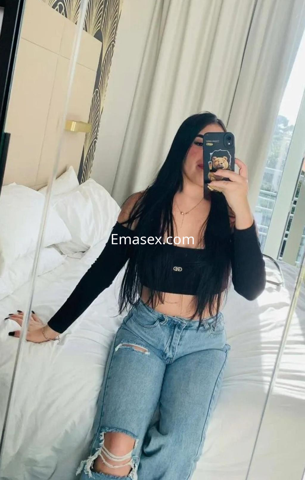 Puta de cabello largo y oscuro, viste una blusa negra y jeans rasgados, posando en una habitación moderna en Tarragona.