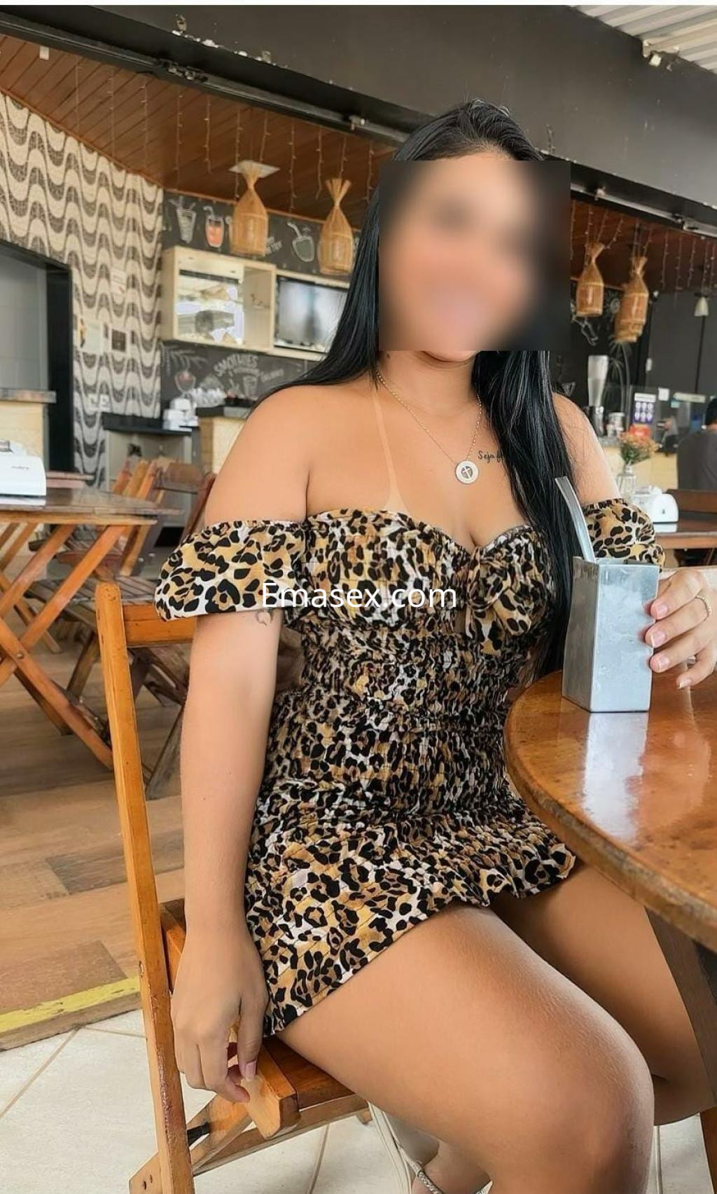 Puta sentada en una silla, lleva un vestido de estampado de leopardo y sostiene un vaso en un ambiente de bar en Santander.