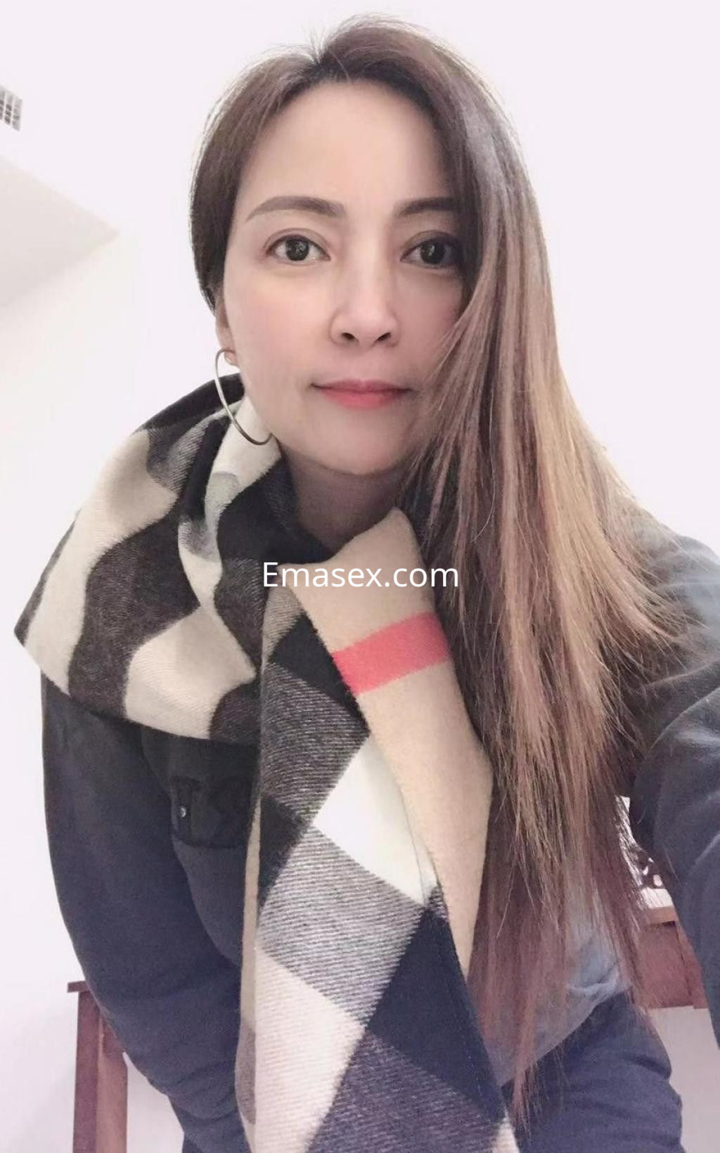 Puta en Barcelona, con cabello largo y lacio, vistiendo un abrigo oscuro y una bufanda de cuadros en tonos claros.