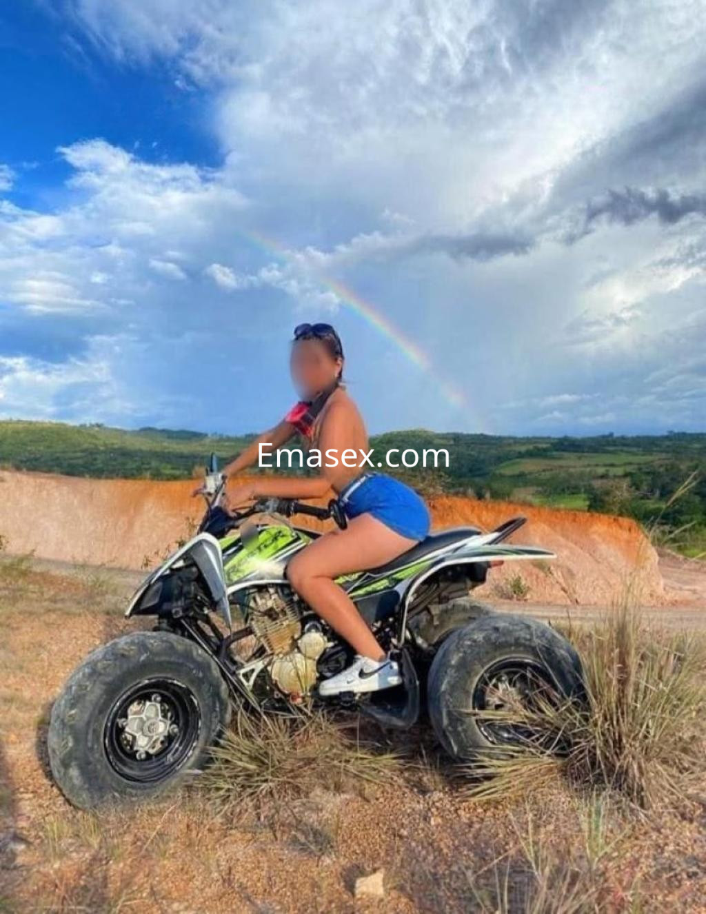 Puta en Huelva monta un quad en un paisaje natural, luciendo un top negro y shorts cortos azules.