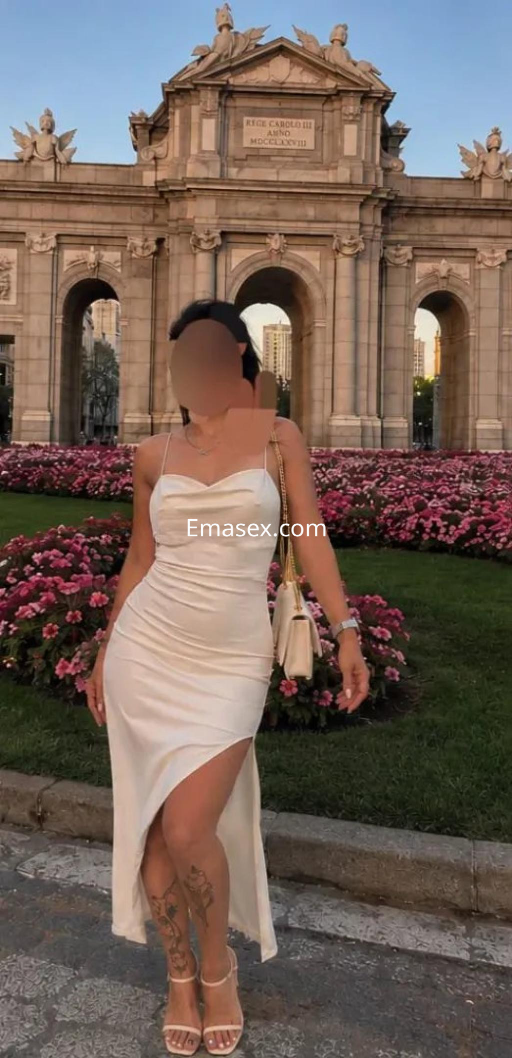 Puta con vestido blanco ajustado y abertura lateral, posando frente a un monumento en Murcia.