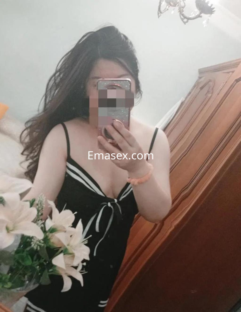 Escort en Salamanca con cabello largo y oscuro, luciendo un vestido negro con tirantes y sosteniendo flores.