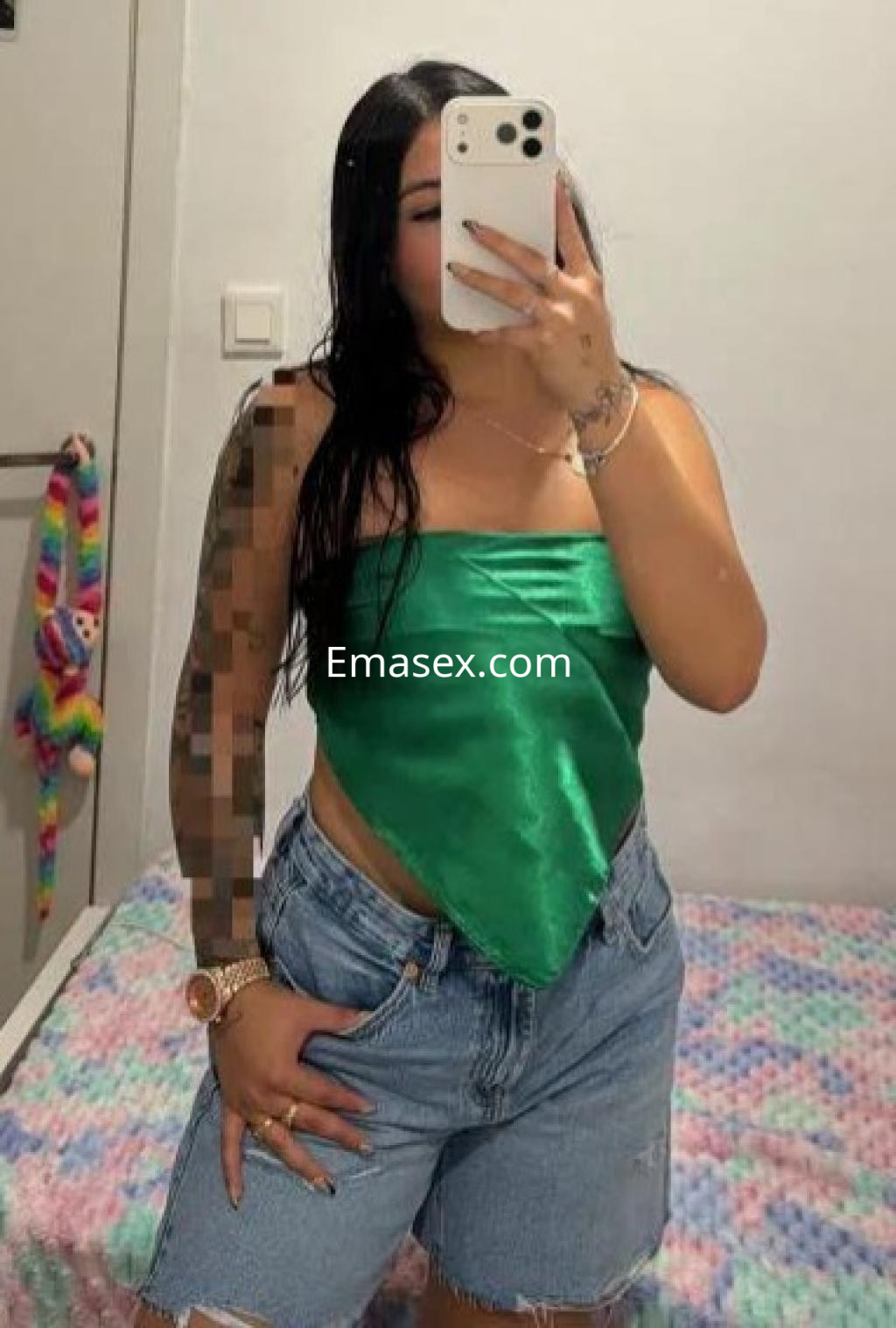 Escort en Tarragona posando frente al espejo con top verde y shorts de mezclilla, mostrando un estilo casual.