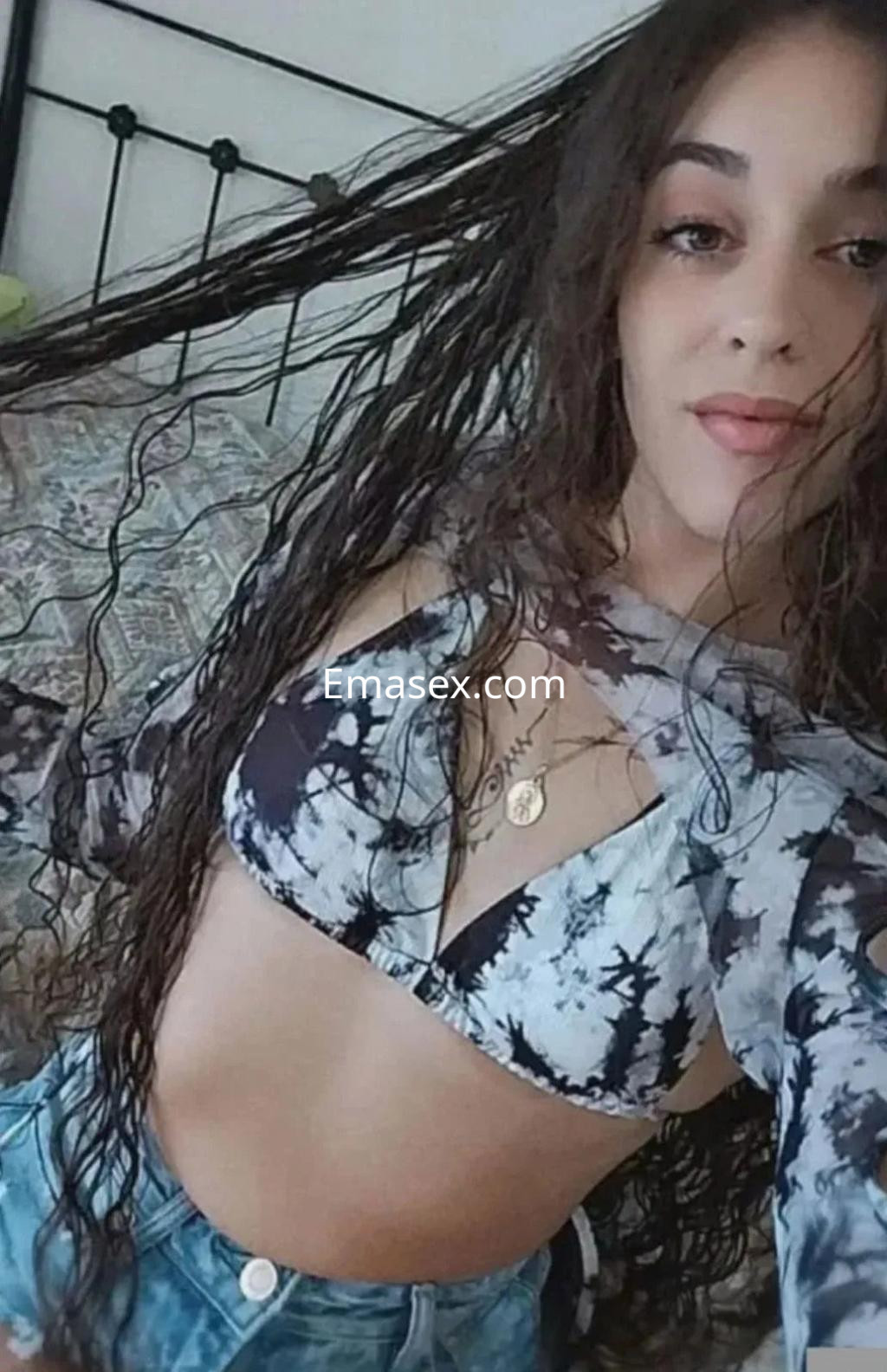 Escort en Sevilla con cabello rizado y suelto, vistiendo un top de estampado y shorts, posando en un ambiente acogedor.