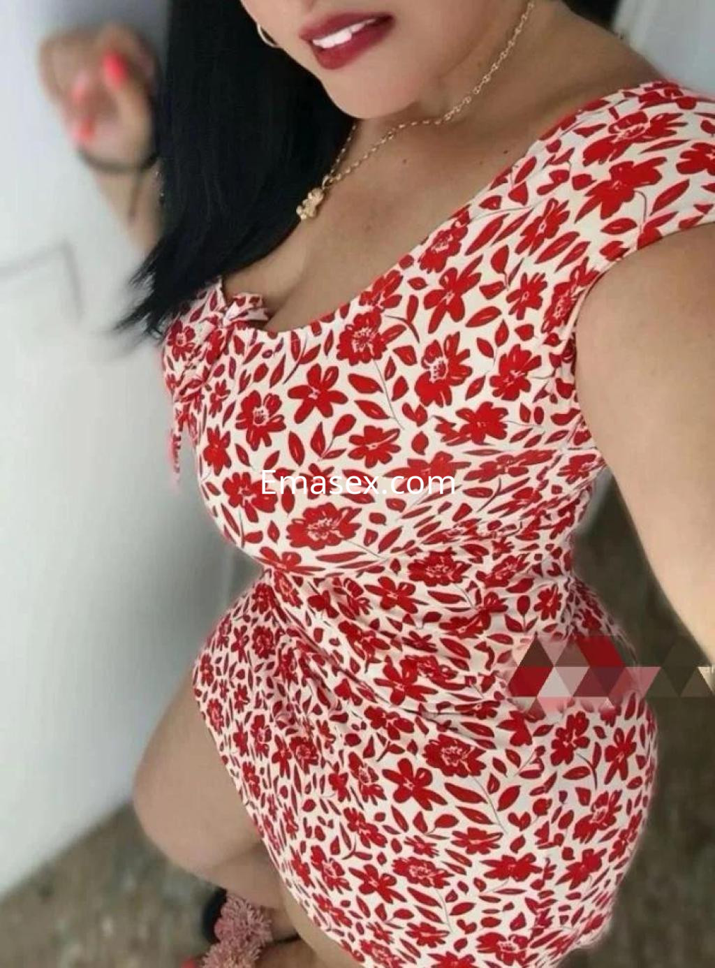 Escort en Badajoz vistiendo un vestido ajustado de flores rojas, con cabello largo y oscuro, sonriendo a la cámara.