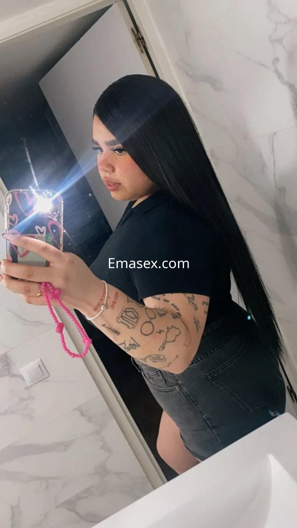 La puta de Granada posa en un espejo con camiseta negra y falda de mezclilla, mostrando su cabello largo y lacio.