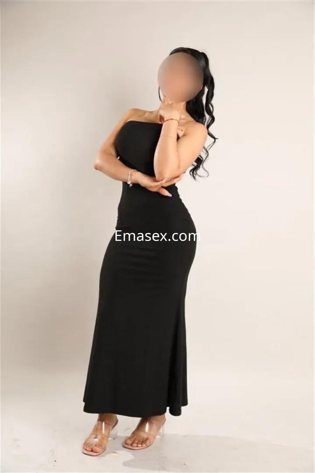 Puta de Cádiz luce un vestido negro ajustado, posando con una mano en la cadera y una sonrisa sutil.
