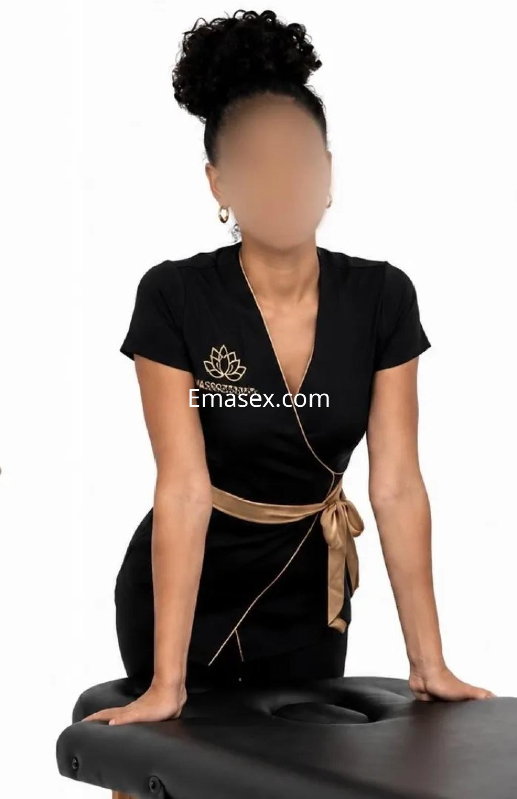 Escort en Valencia con cabello rizado, viste un vestido negro ajustado y un cinturón dorado, apoyada en una mesa.