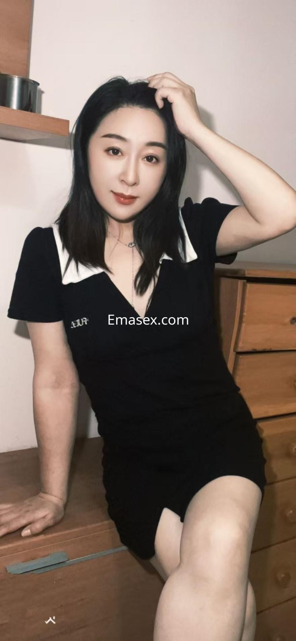 Puta posando en un vestido negro ajustado con detalles en el cuello, en un entorno doméstico en Oviedo.