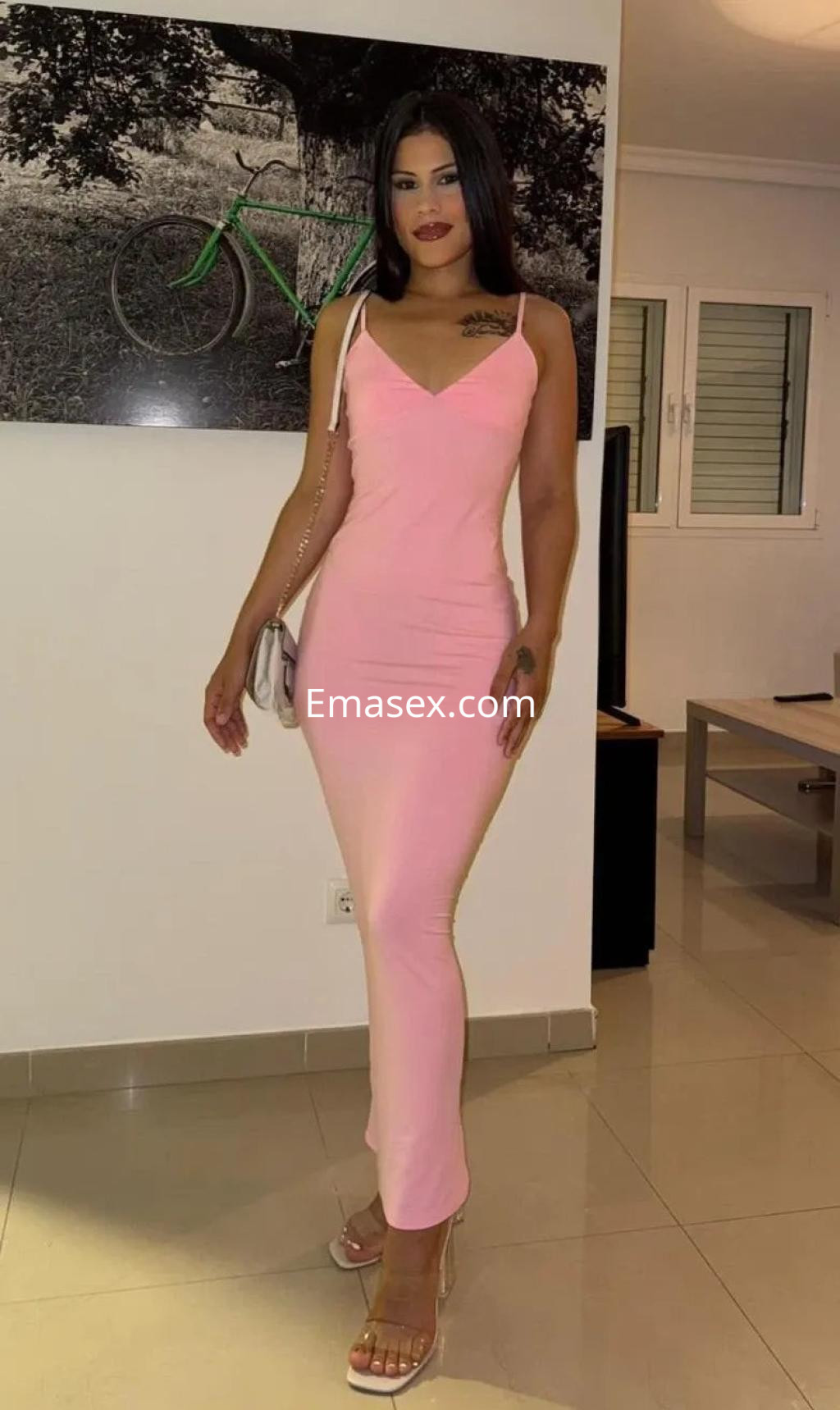 Puta en Alicante luce un vestido ajustado color rosa y sandalias transparentes en un ambiente interior.