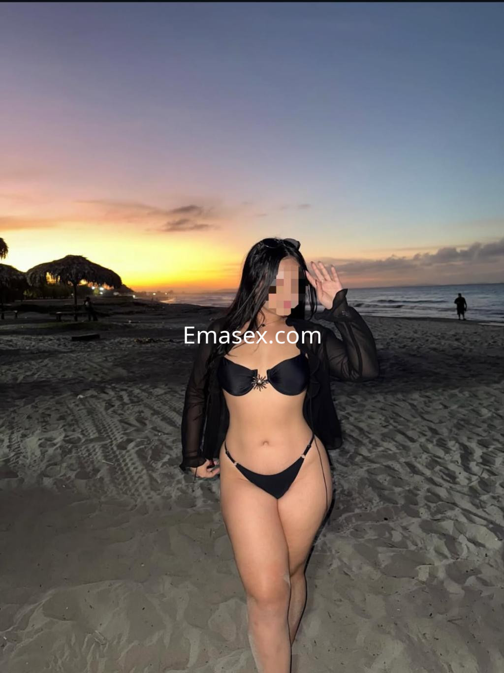 Escort en Santiago con cabello largo y oscuro, vistiendo un bikini negro mientras camina por la playa al atardecer.