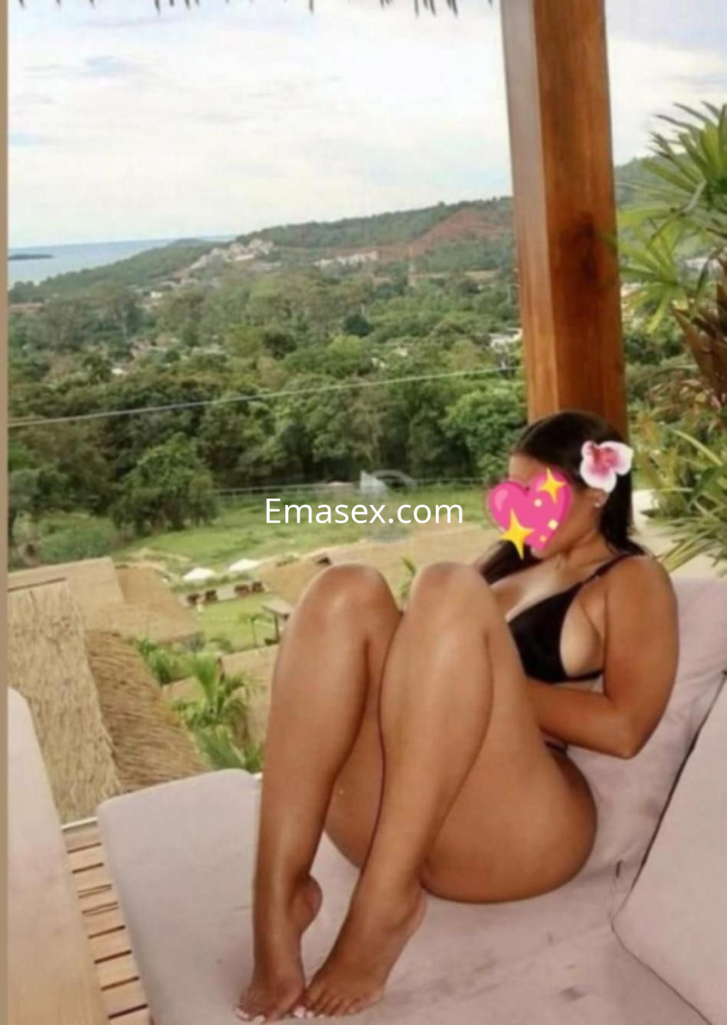 Puta sentada en un sofá al aire libre en Pontevedra, luciendo un bikini negro y con un paisaje verde de fondo.