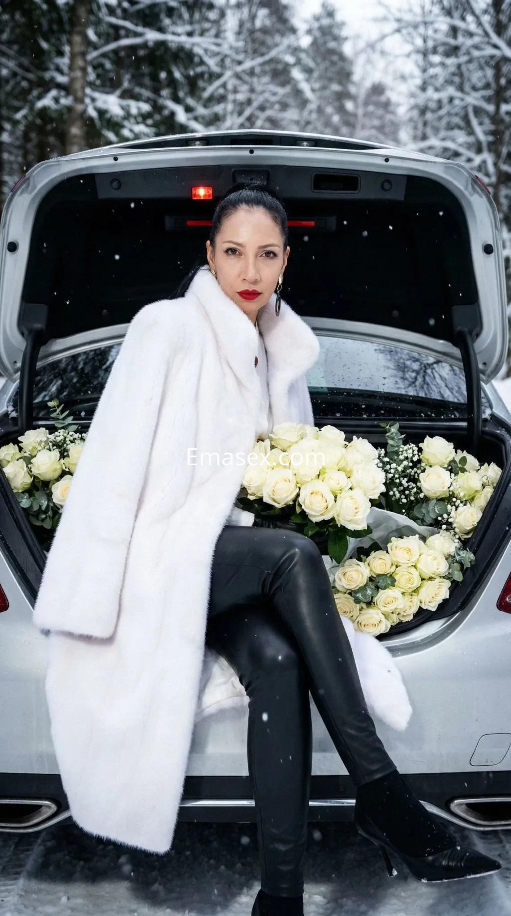 Escort en Alicante sentada en el maletero de un coche, vistiendo un abrigo blanco y leggings negros, rodeada de rosas blancas.