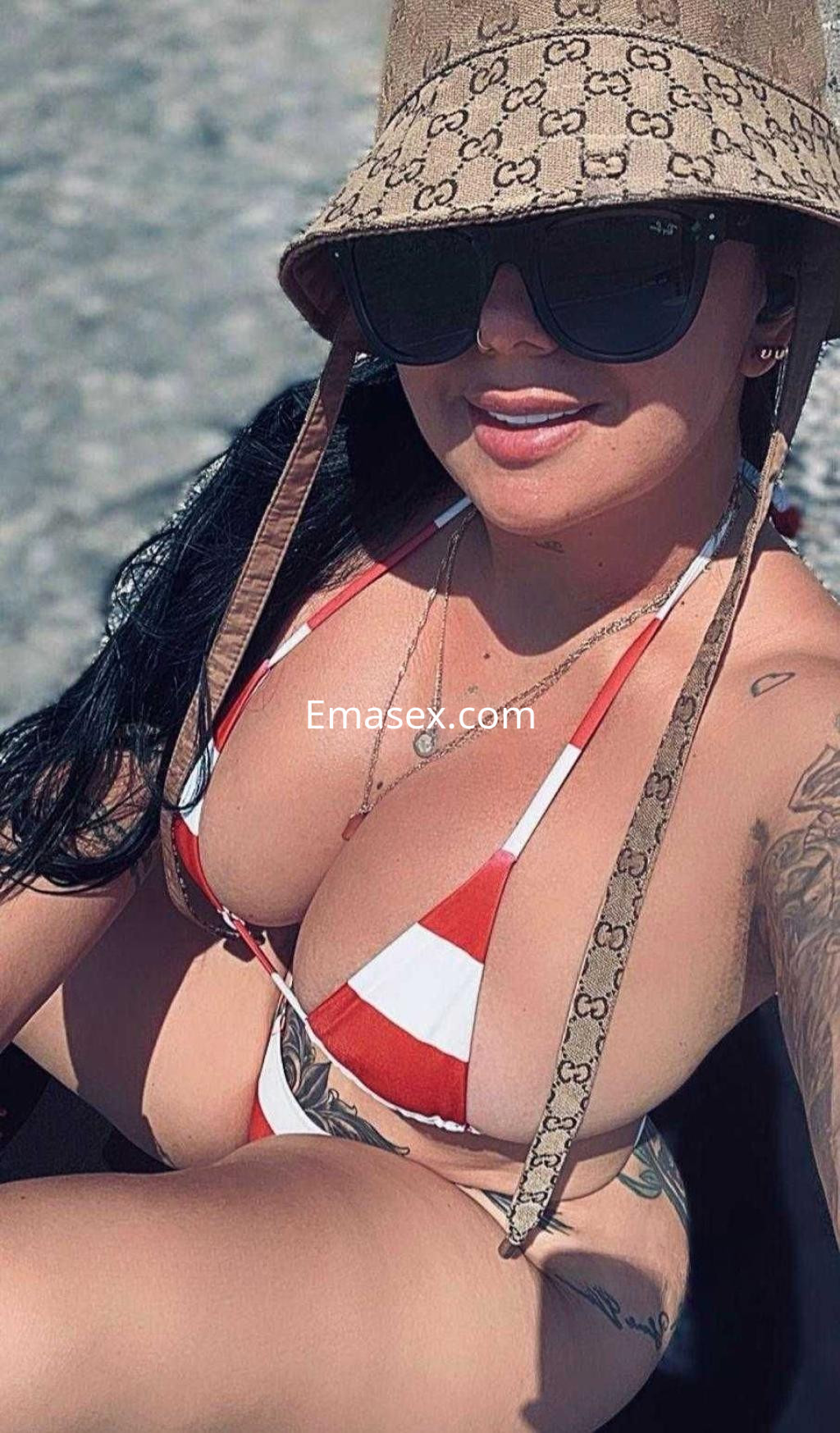 Puta sentada en la playa de Huelva, con un bikini de rayas rojas y blancas, sombrero y gafas de sol.