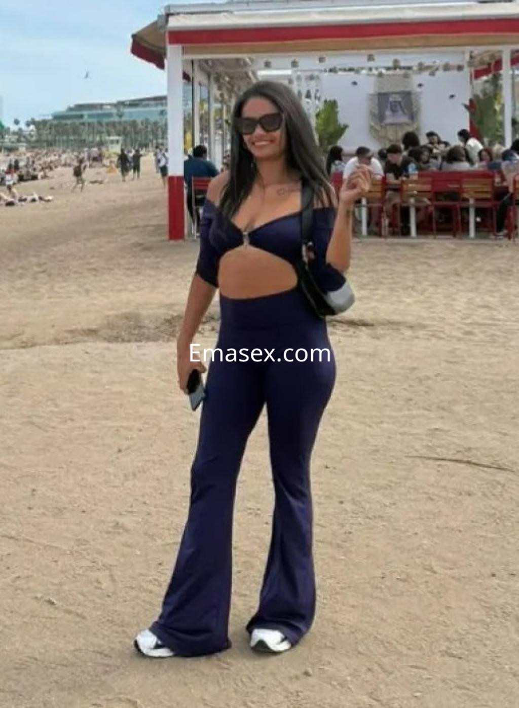 Escort en Barcelona viste un conjunto azul ajustado con abertura en el abdomen, posando en la playa.
