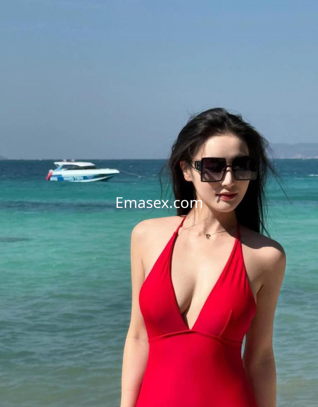 Puta con traje de baño rojo posando en la playa de Palma de Mallorca, con el mar y un barco de fondo.