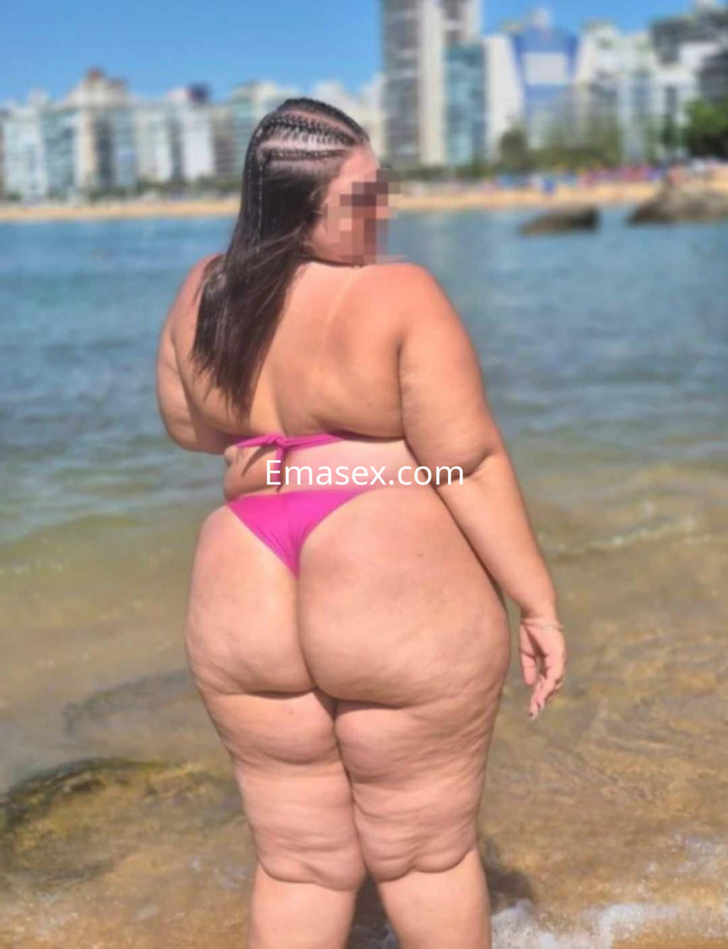 Puta con cabello largo y trenzado, usando un bikini rosa en la playa de León, disfrutando del sol y el mar.