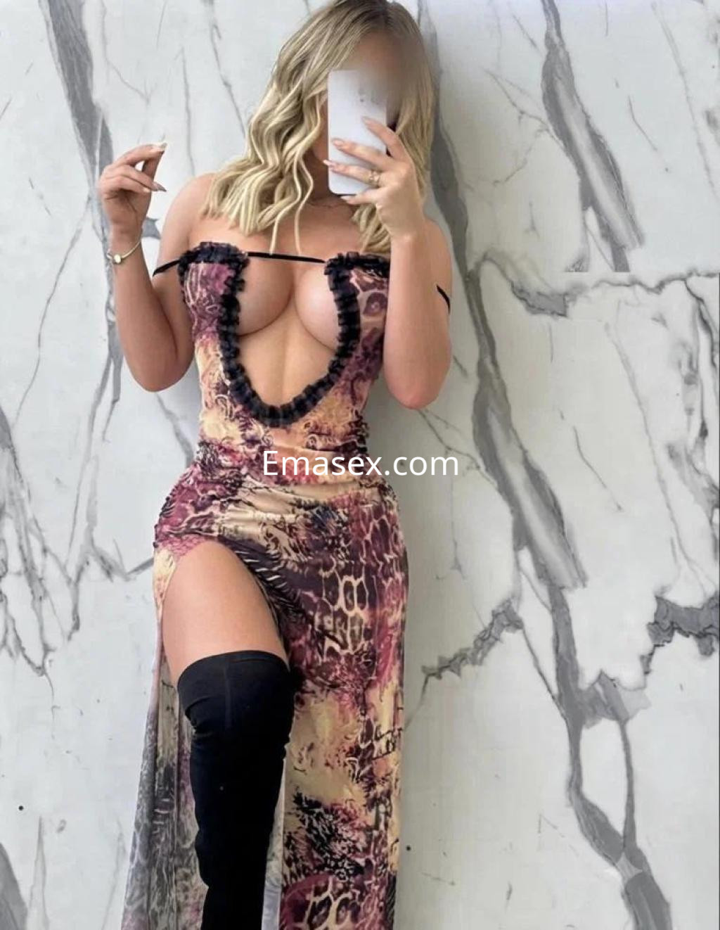 Escort en Málaga con un vestido largo de estampado animal y abertura lateral, posando frente a un espejo.