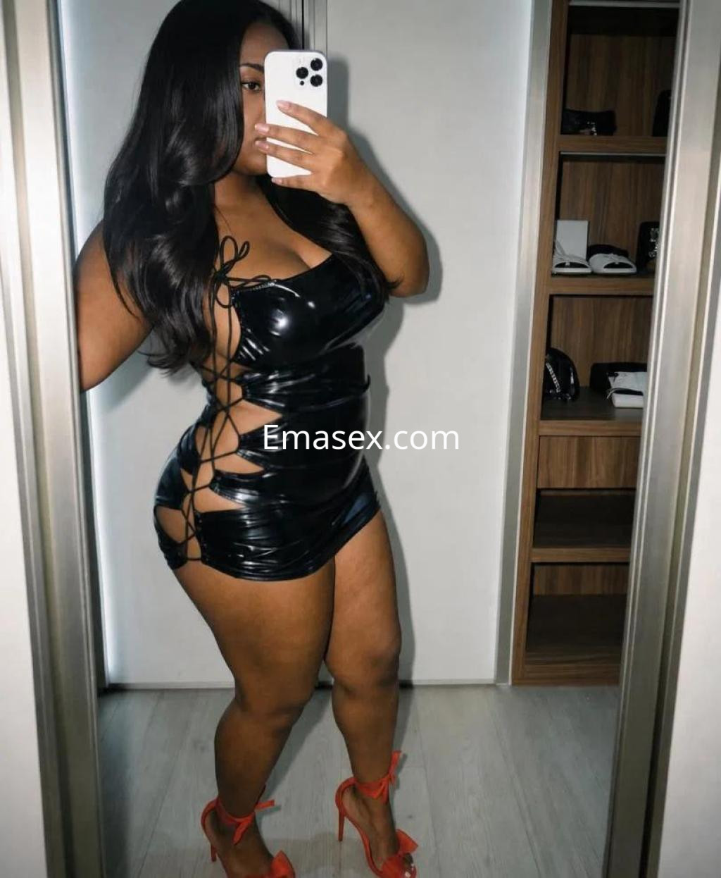 Escort en Córdoba luciendo un vestido de látex negro ajustado con detalles de encaje, y tacones rojos.