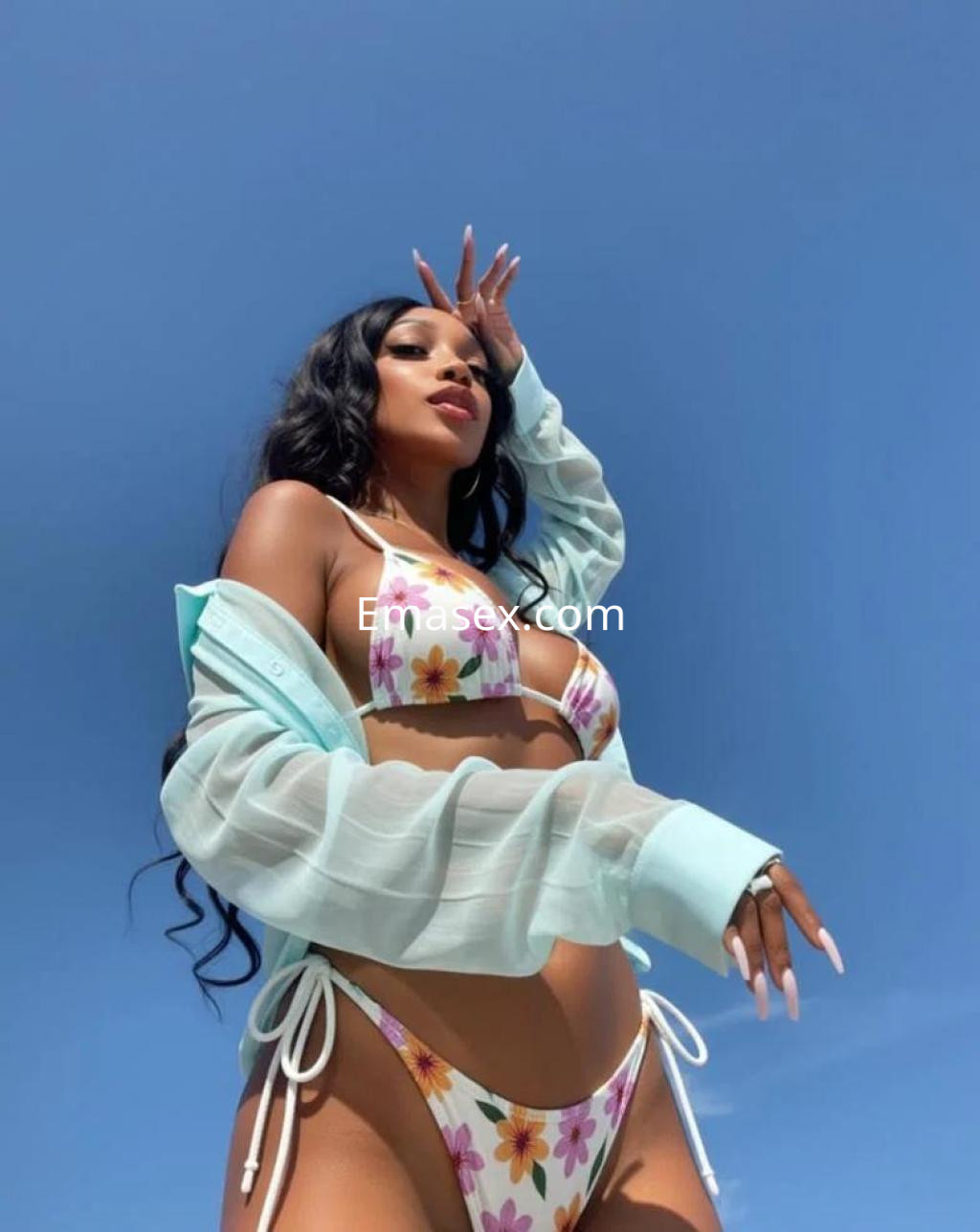 La puta luce un bikini floral con una camisa ligera, posando bajo un cielo despejado en Girona.