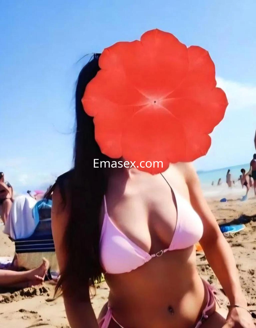 Escort en la playa de Coruña, luciendo un bikini rosa, con cabello largo y una postura relajada.