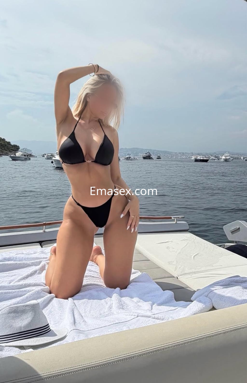 Escort en Tenerife, posando en un yate con bikini negro, frente a un paisaje marítimo y soleado.
