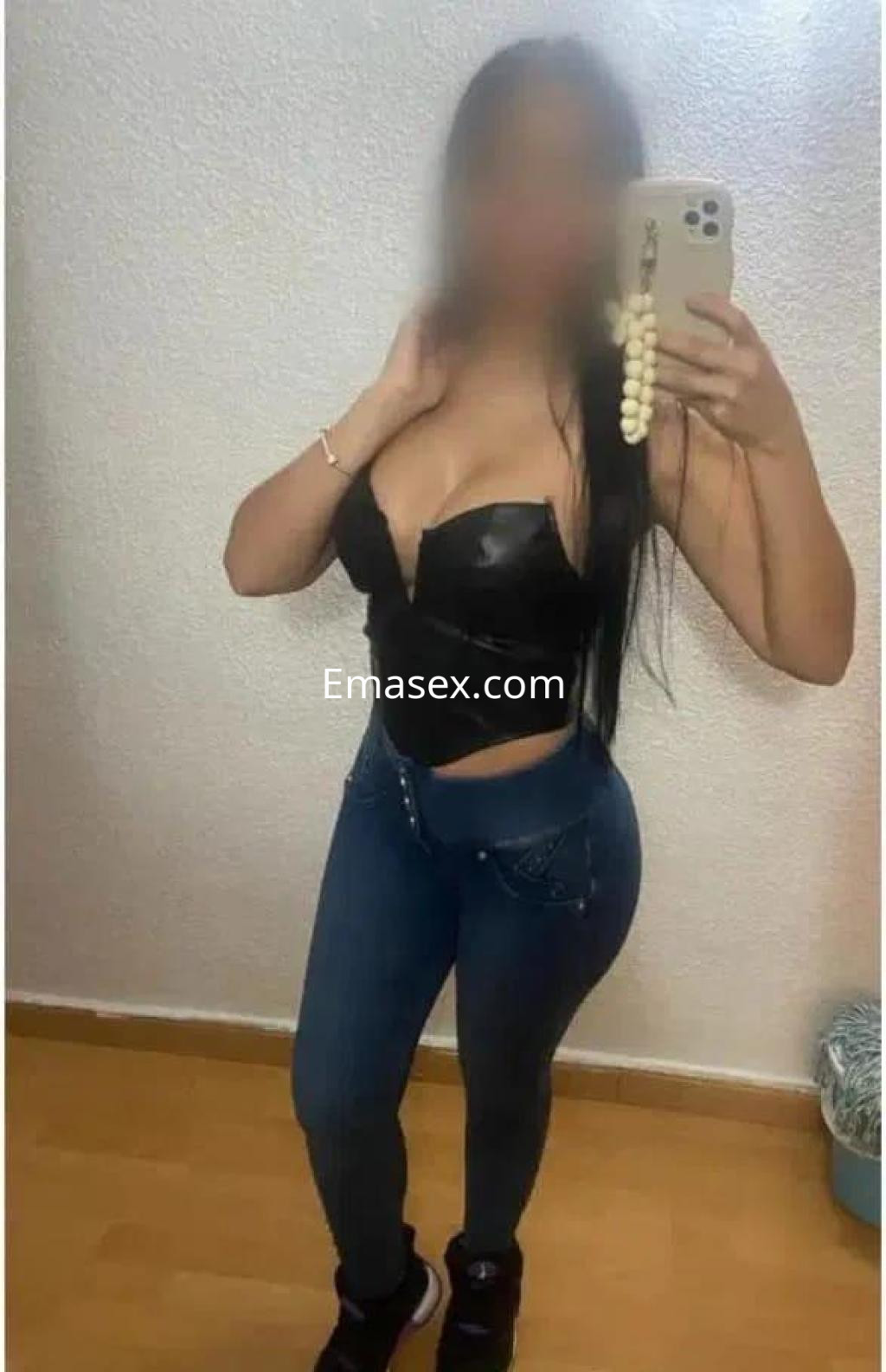 Escort en Zamora posando frente al espejo con blusa negra ajustada y jeans, mostrando su figura.