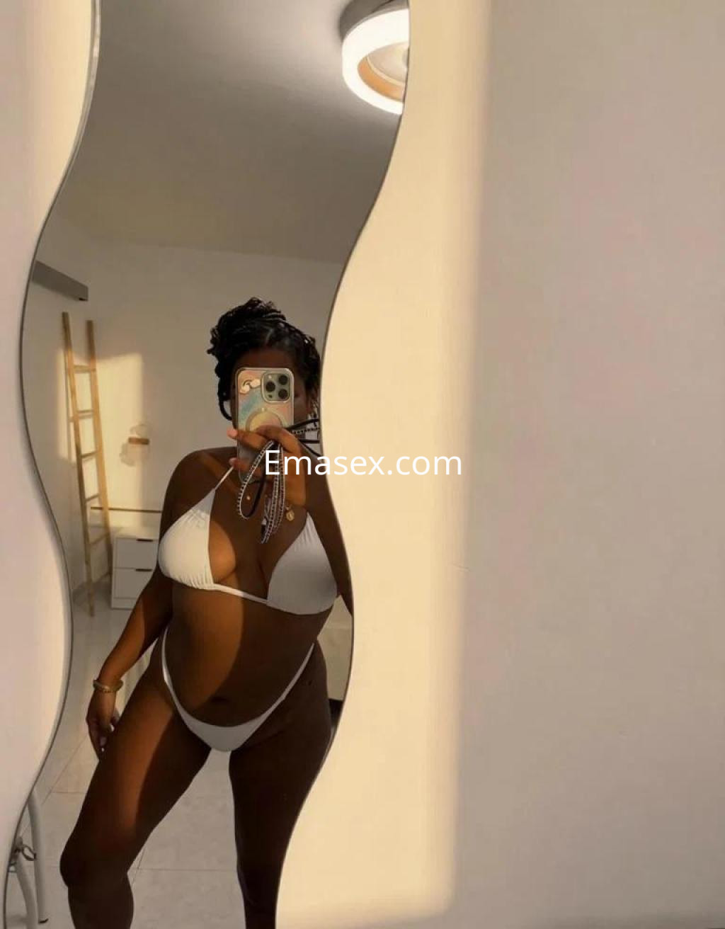 Escort en Cádiz con bikini blanco, posando frente a un espejo con luz suave y fondo claro.