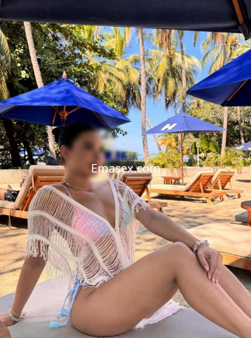 Puta en Cádiz, lleva un pareo blanco con flecos y un bikini colorido, relajándose en un entorno de playa.