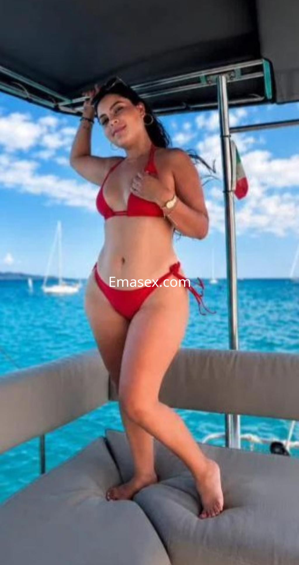 Escort en Málaga, posando en un yate con un bikini rojo, bajo un cielo despejado y mar azul.