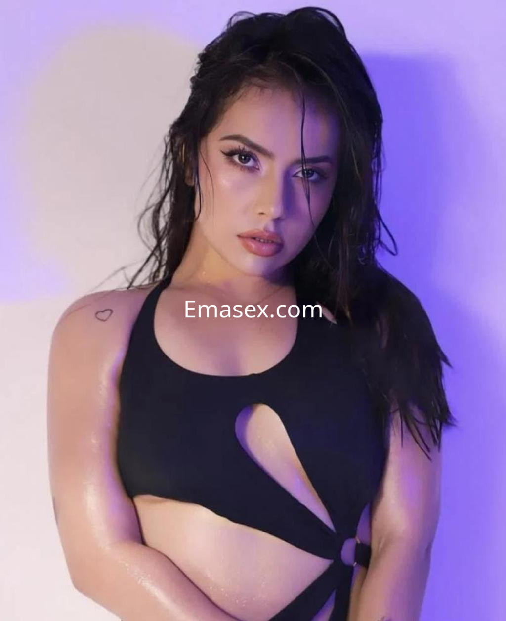 Escort en Sevilla con cabello oscuro y húmedo, vistiendo un top negro con corte, mirada intensa y fondo iluminado.