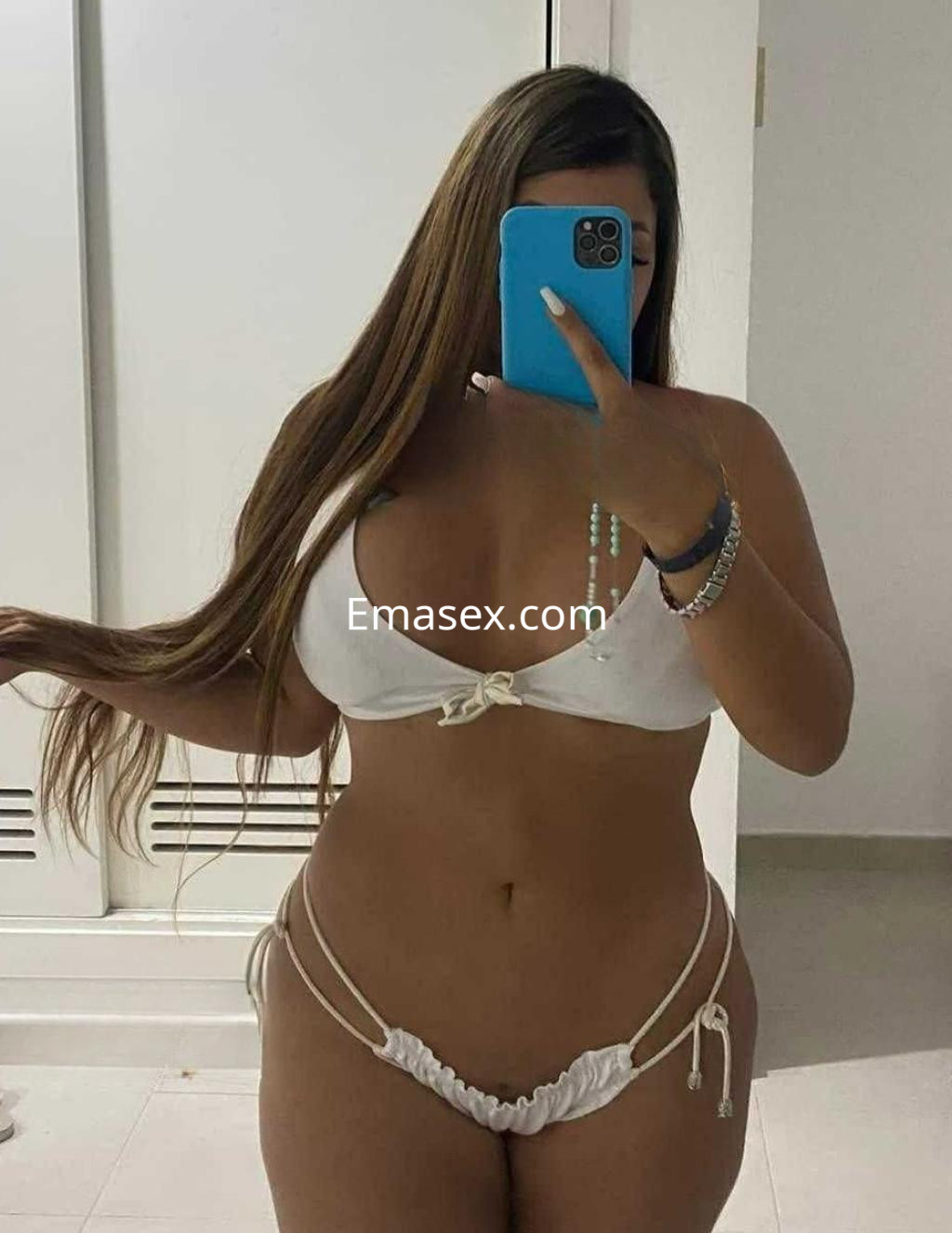 Escort en Zaragoza con cabello largo y lacio, usando un bikini blanco mientras se mira en el espejo.