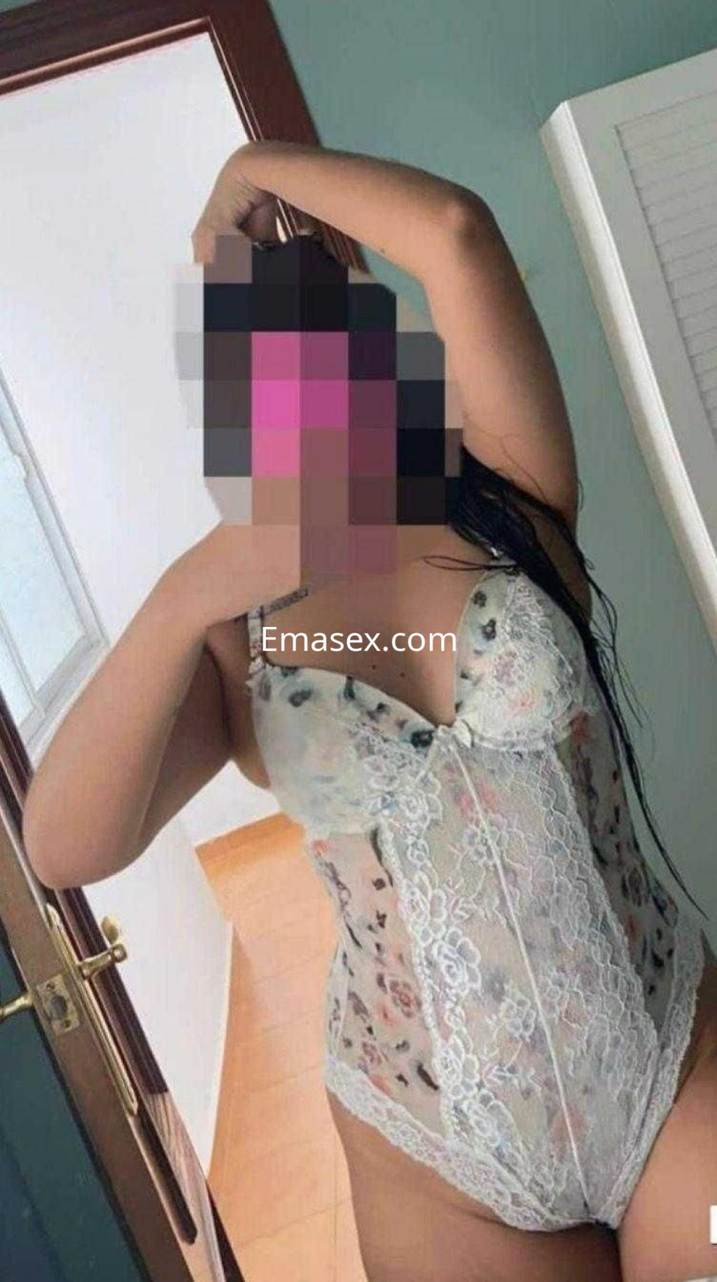Puta en Zaragoza viste un body de encaje blanco con flores y posa con una mano en el cabello.