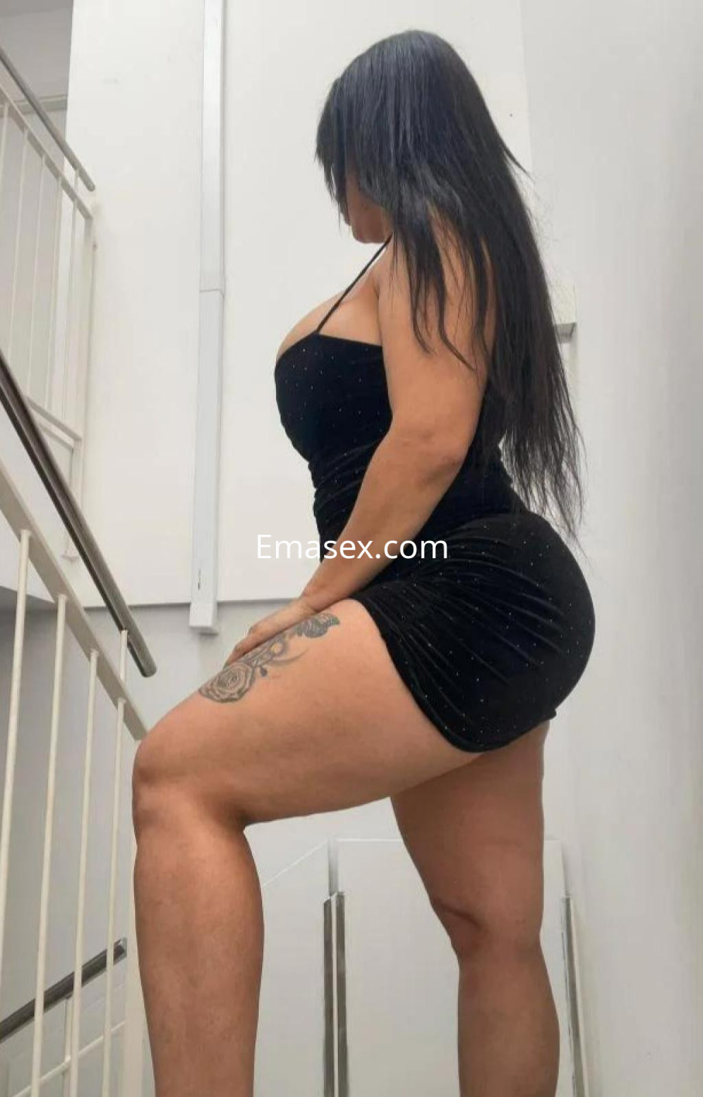 Puta en Barcelona luciendo un vestido negro corto y ajustado, con cabello largo y una pose seductora en la escalera.